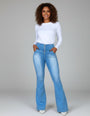 Mulher usando calça flare jeans modeladora de cintura alta e blusa branca, em fundo neutro.