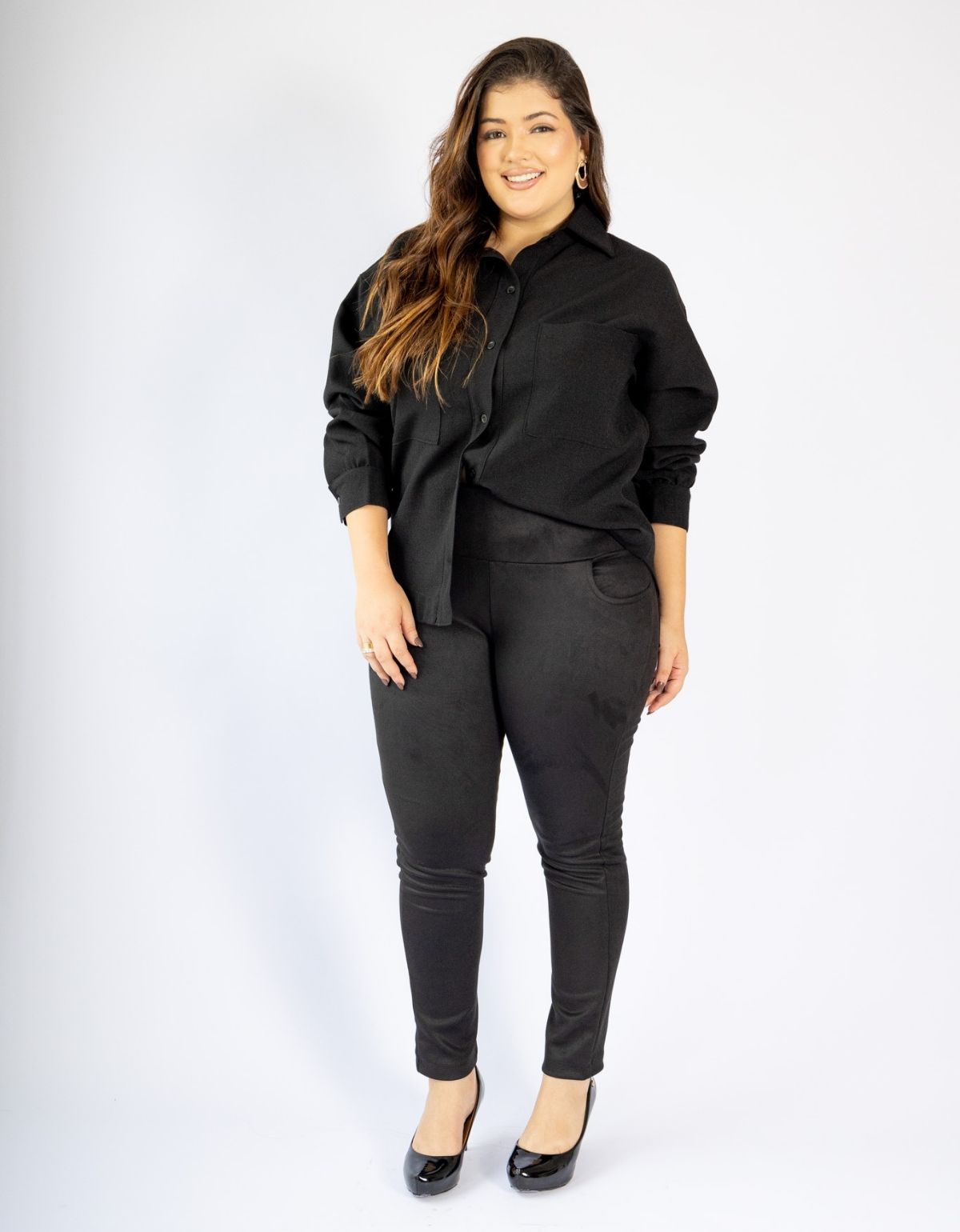 Mulher usando conjunto modelador preto com calça skinny e camisa, em fundo branco, moda plus size.