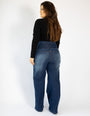 Mulher vestindo calça jeans modeladora de cintura alta, vista de costas, em fundo branco.