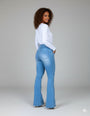 Mulher usando calça jeans flare modeladora azul claro e blusa branca, vista de costas.
