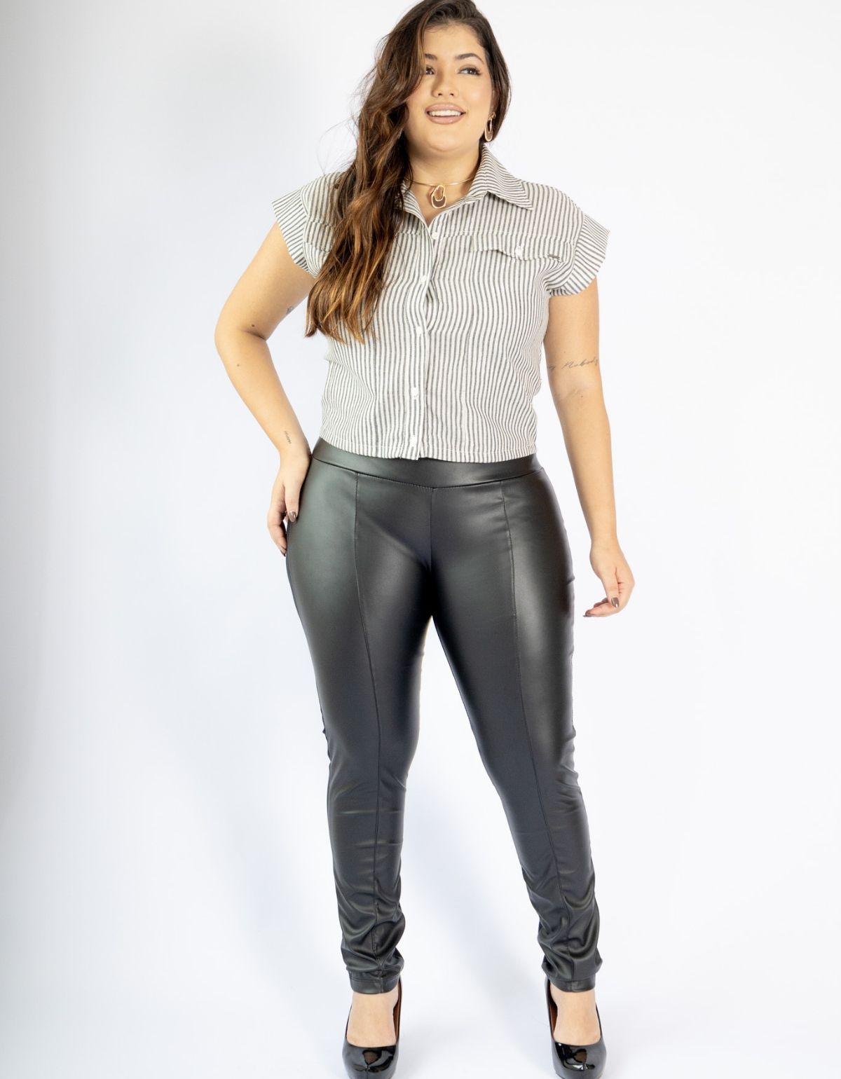 Mulher usando calça modeladora preta de couro ecológico e blusa listrada, moda plus size.