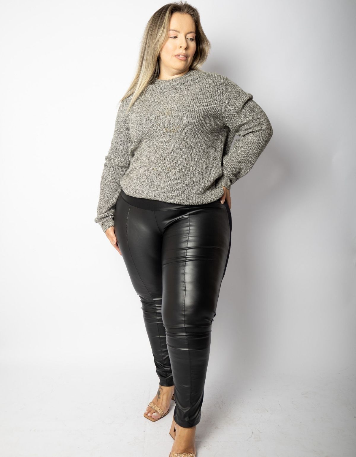Mulher vestindo calça modeladora preta de courino e suéter cinza, moda plus size.