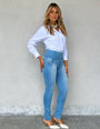 Mulher usando calça jeans modeladora de cintura alta e camisa branca, moda feminina.