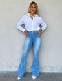 Mulher usando calça modeladora jeans flare de cintura alta e camisa branca, estilo casual.