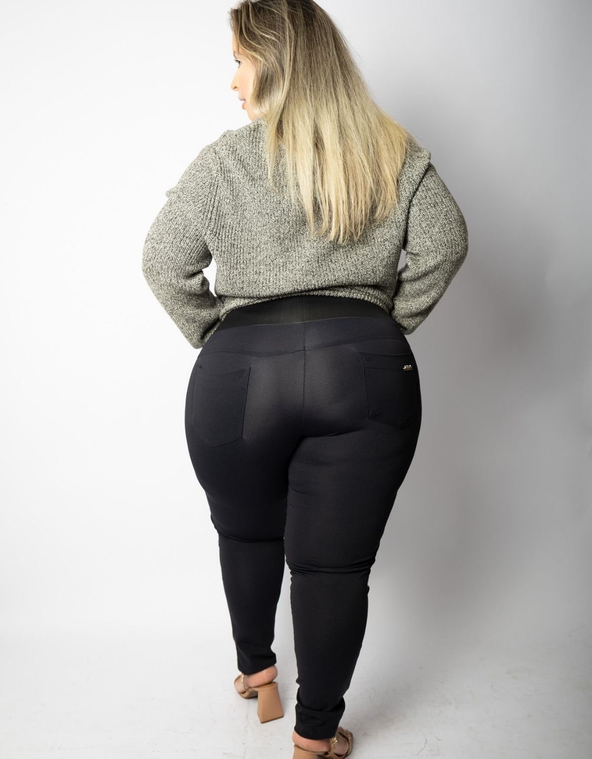 Mulher de costas vestindo calça modeladora preta e suéter cinza, moda plus size