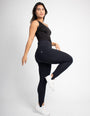 Mulher vestindo calça modeladora preta de cintura alta e blusa preta, posando em estúdio.